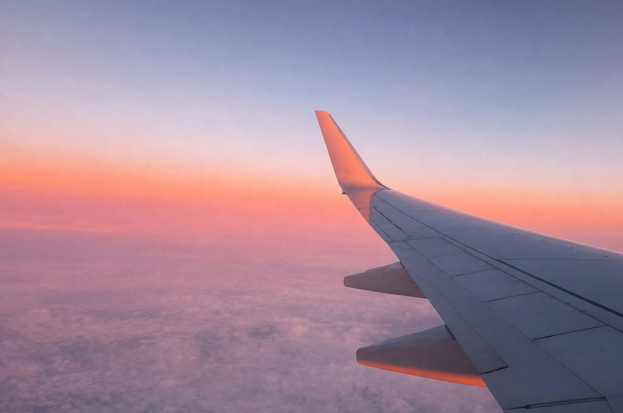 An aeroplane wing tip against a pink and lavender sunset sky