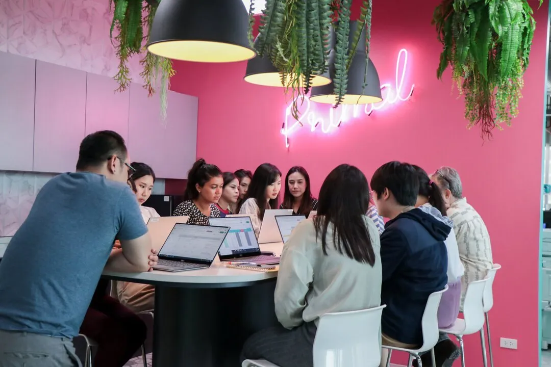 Primal team members in a meeting around a long table with laptops, under a pink Primal neon sign