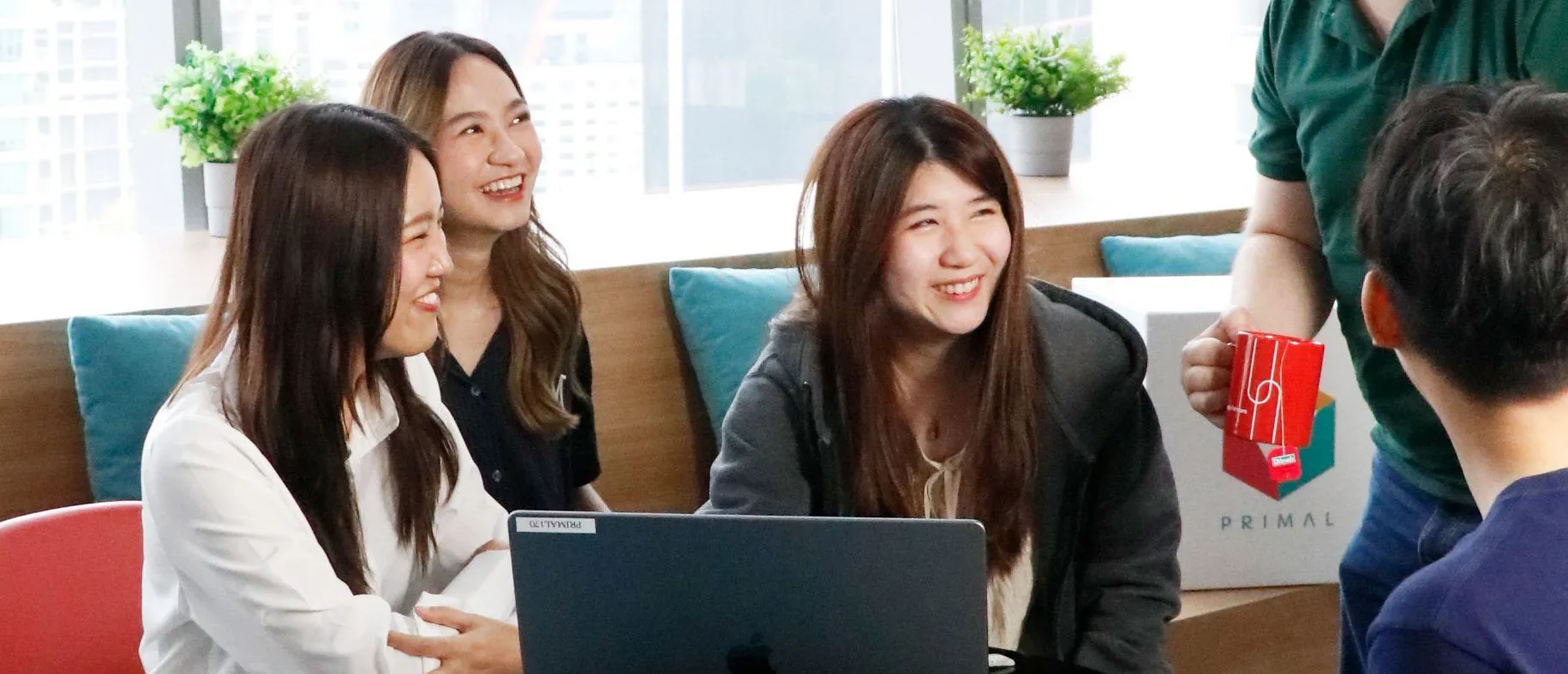 Primal colleagues smiling around a laptop at a table with a Primal mug