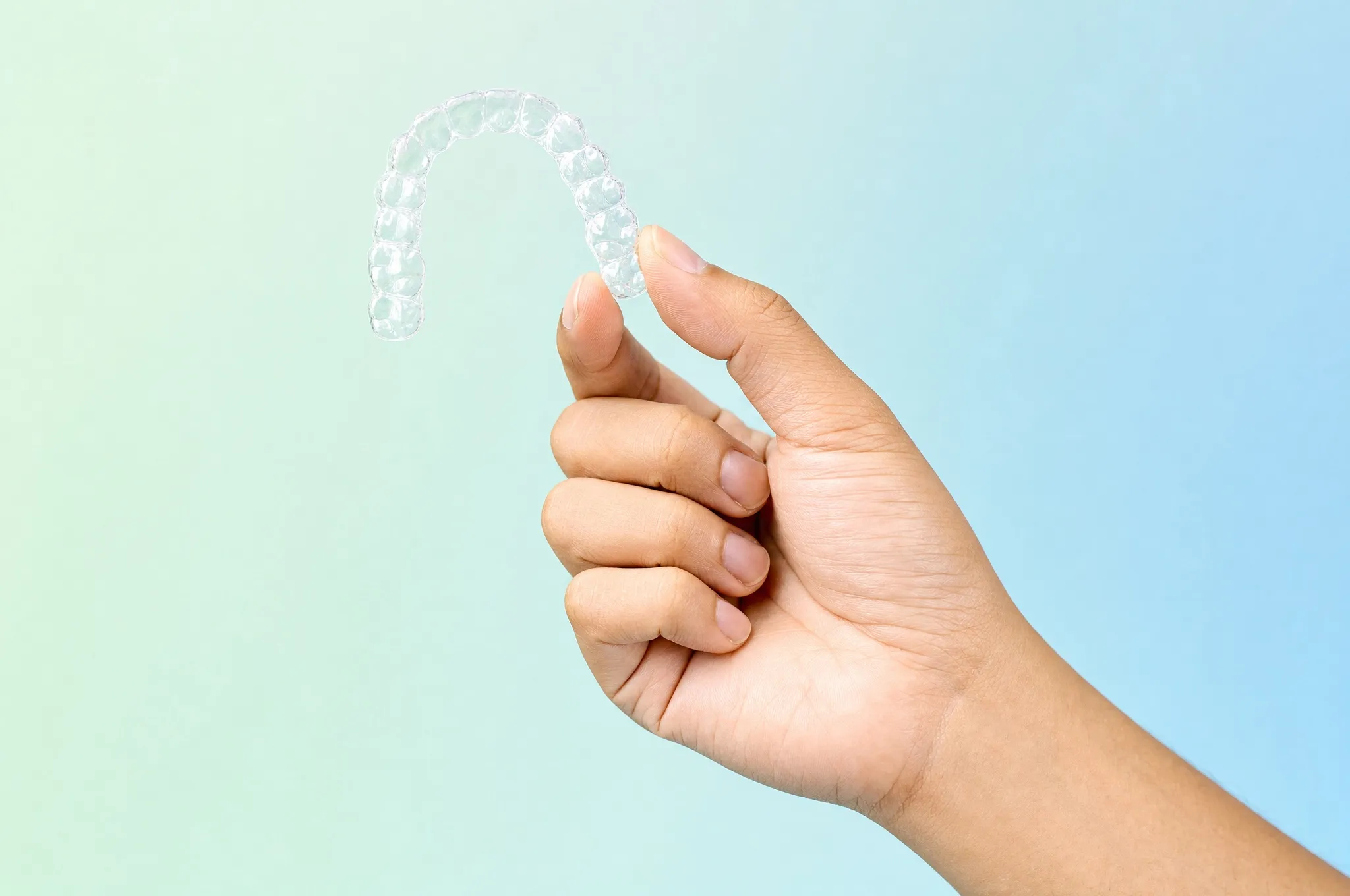 A clear dental aligner held between two fingers