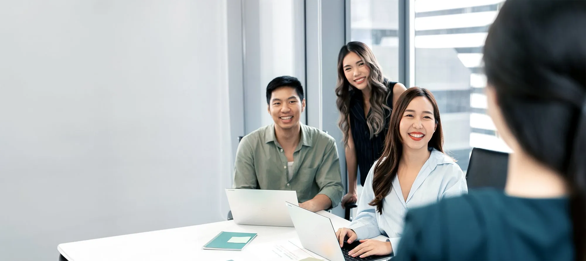 Four colleagues smiling around laptops in a glass-walled meeting room